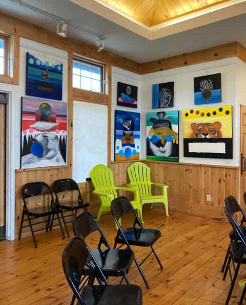 The inside of the Visitor Info Centre. Black folding chairs, big outdoor armchairs, and colorful paintings on the walls